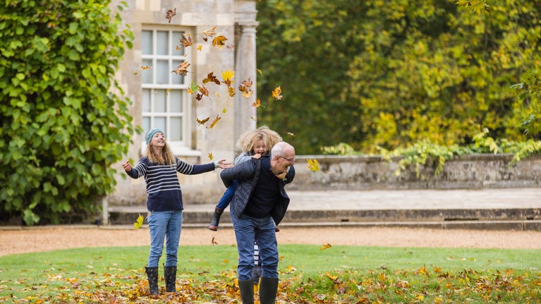 A family playing with autumn leaves outdoors at Mottisfont, Hampshire